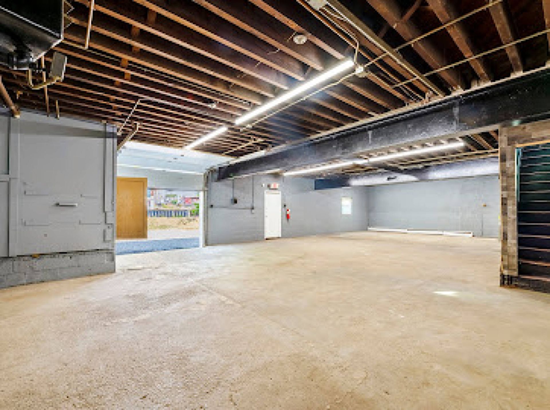 An empty basement with a wooden ceiling and stairs.