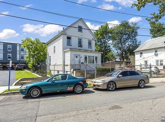 Two cars are parked on the side of the road in front of a house.
