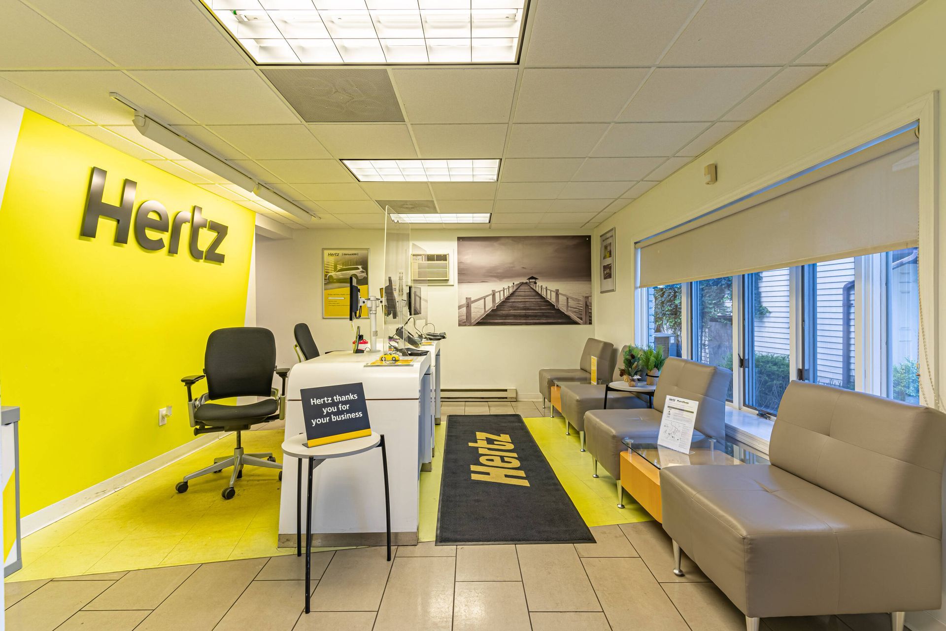 A hertz car rental office with a yellow wall and a couch.