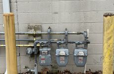 Three gas meters are attached to a brick wall.