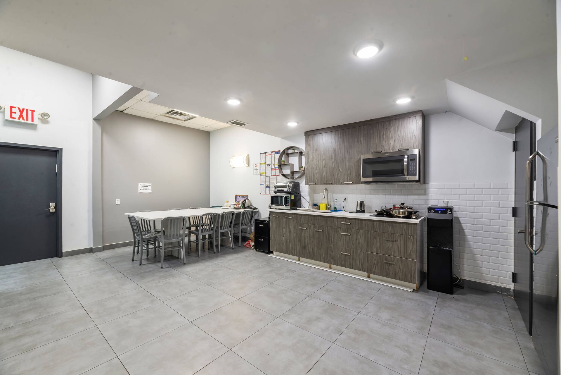 A kitchen with a table and chairs and a red exit sign.