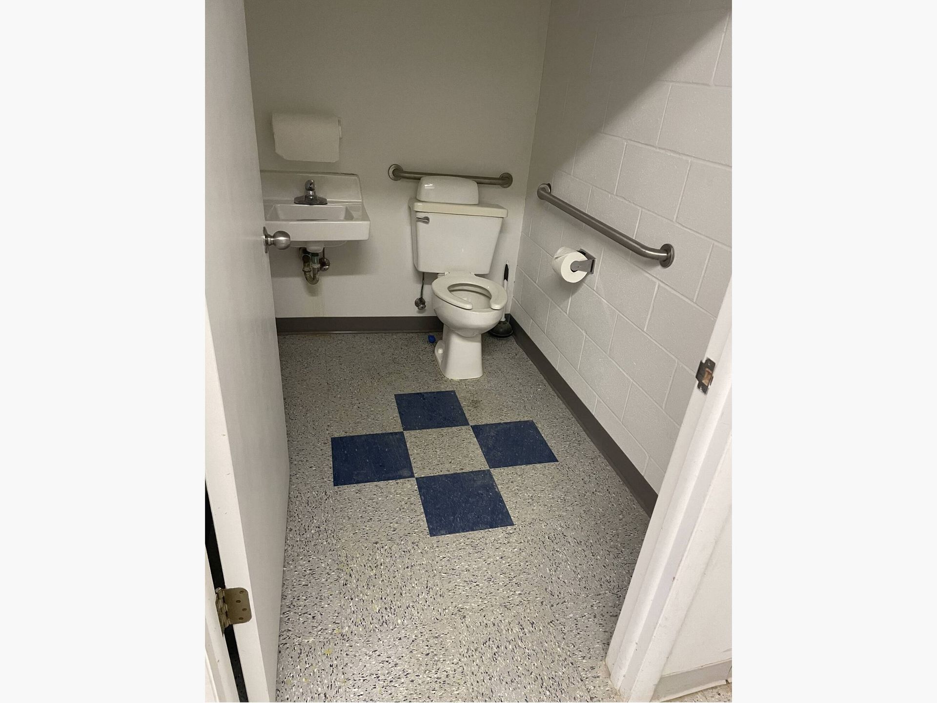 A bathroom with a toilet , sink , and checkered floor.