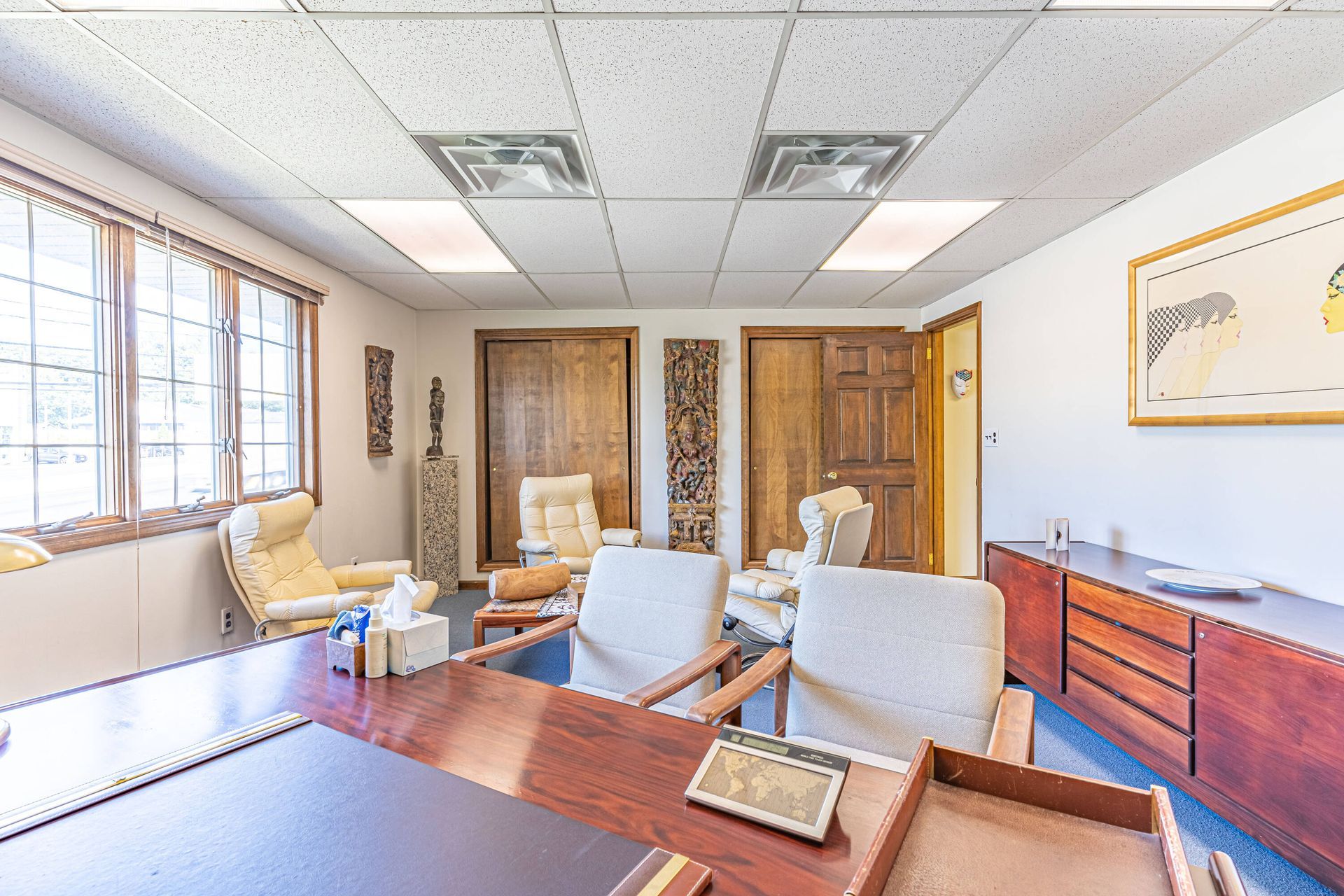 A room with a desk , chairs and a painting on the wall.