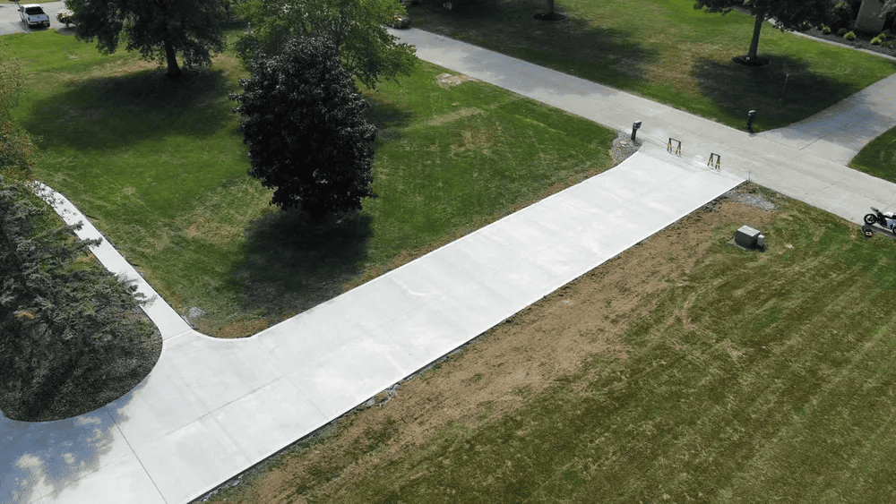 An aerial view of a concrete driveway surrounded by grass and trees.