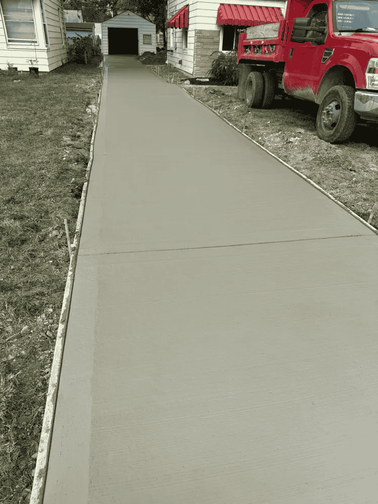 A red truck is parked on the side of a concrete driveway.