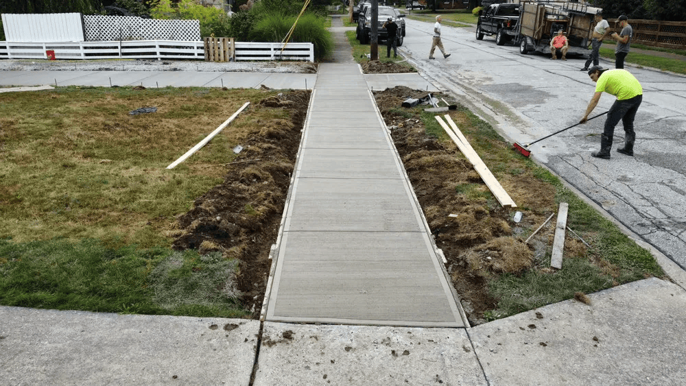 A man is working on a sidewalk in front of a house.
