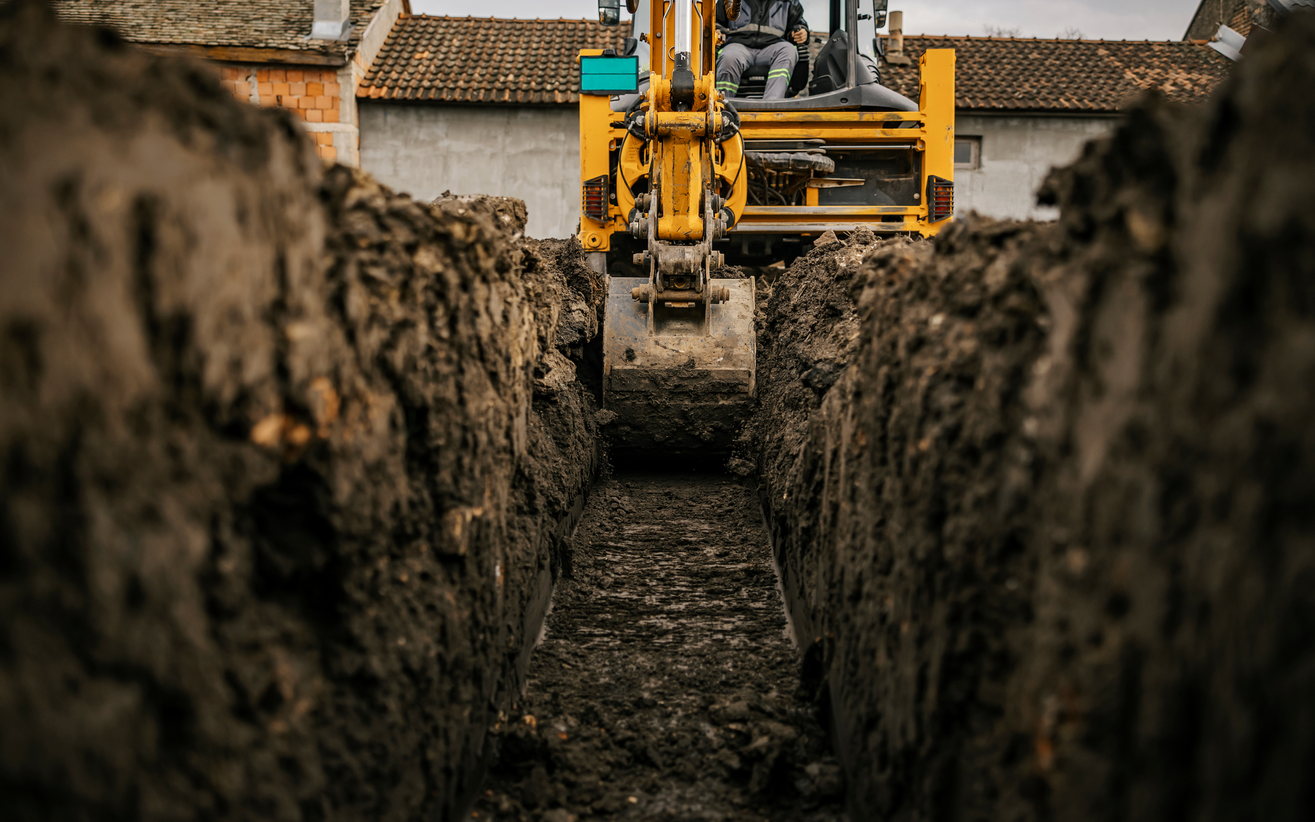 A yellow excavator is digging a trench in the dirt.
