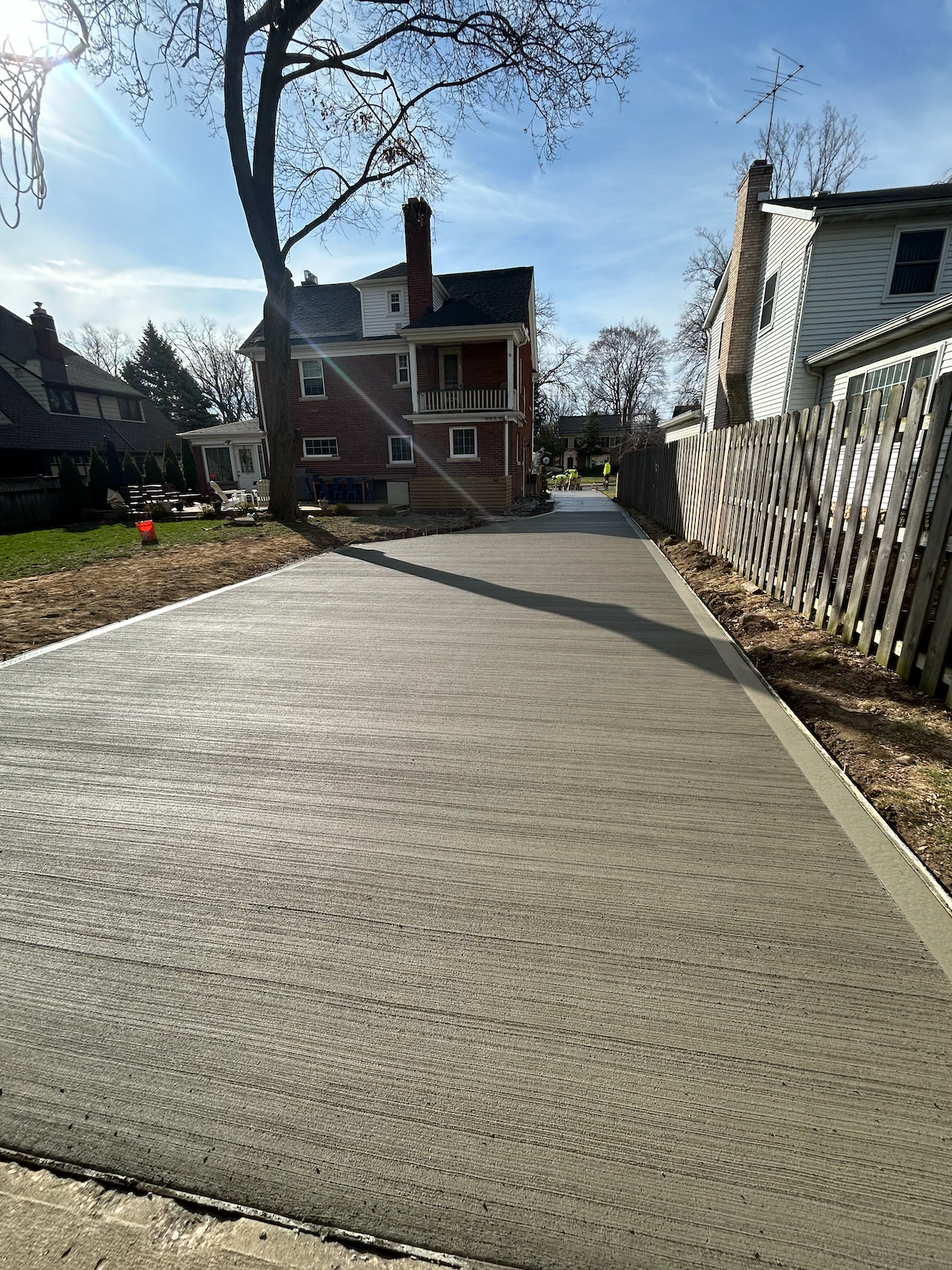 A concrete driveway with a fence and a house in the background.