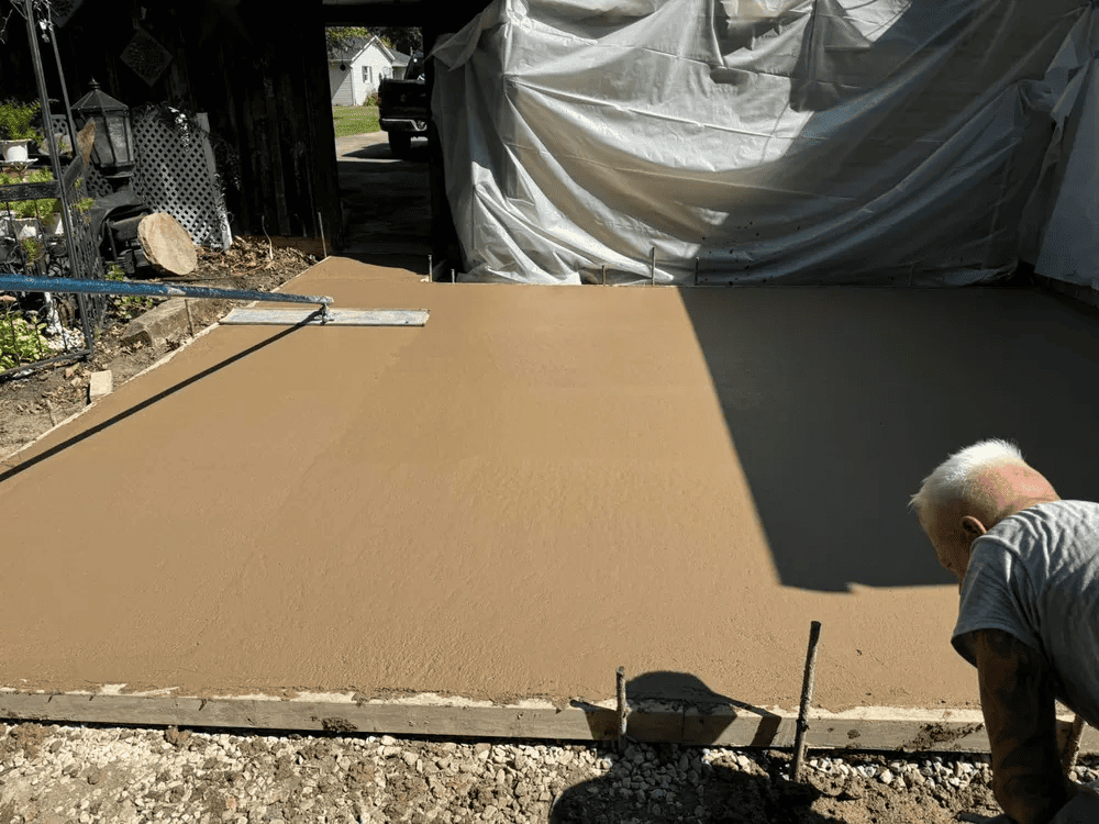 A man is working on a concrete driveway in front of a garage.