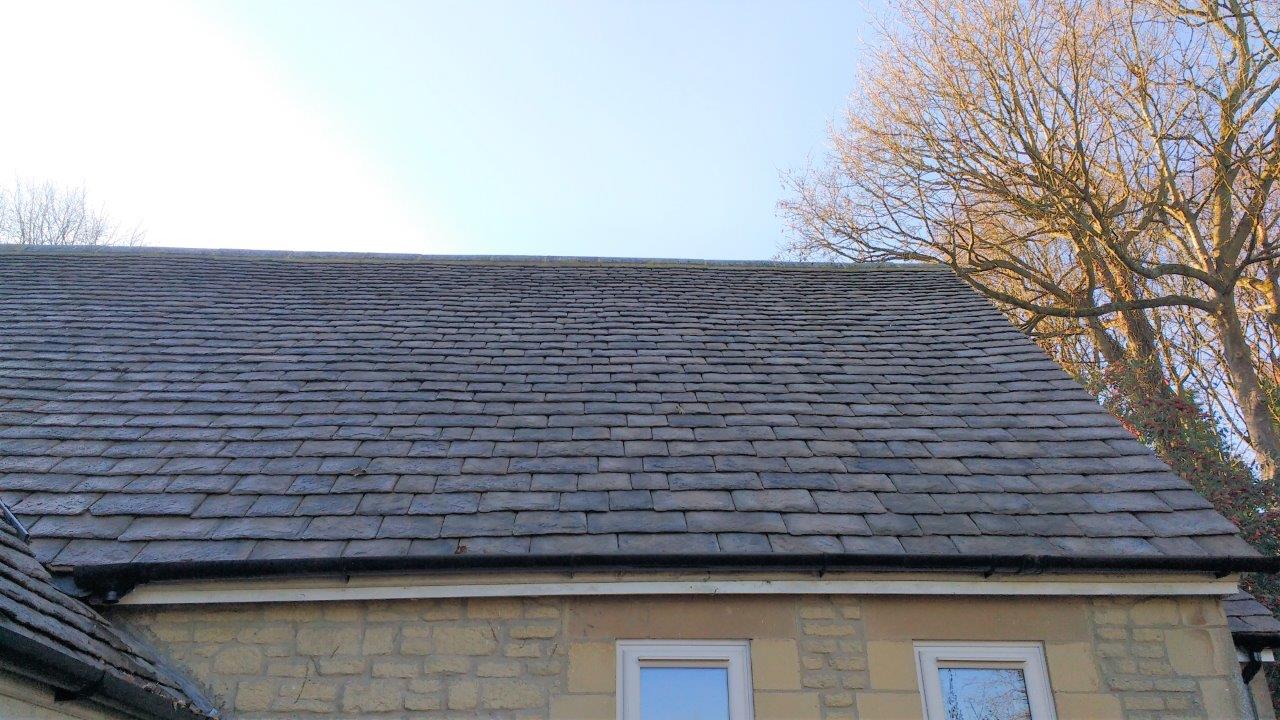 The roof of a house with a slate roof and a tree in the background.