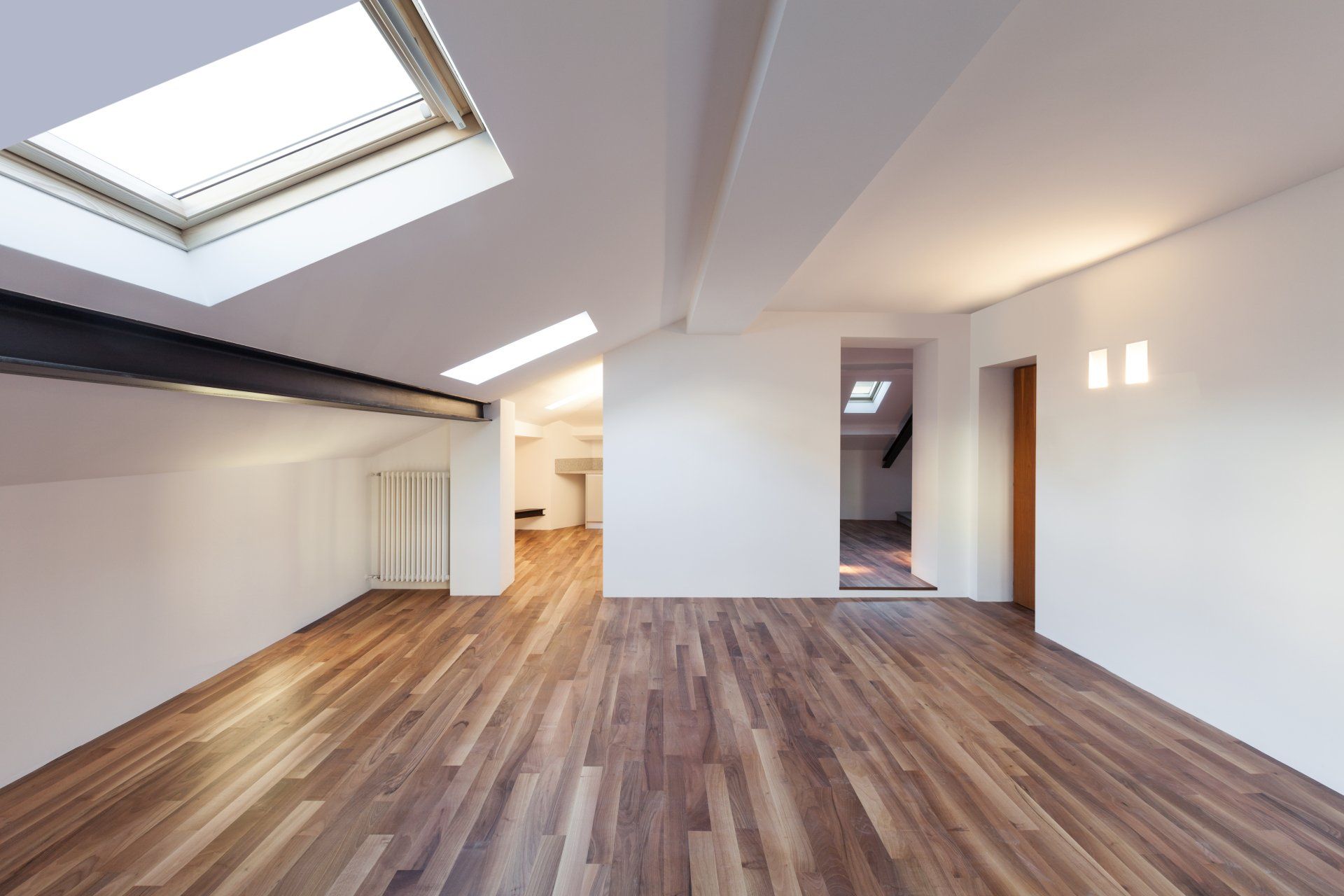 An empty room with hardwood floors and a skylight in the ceiling.