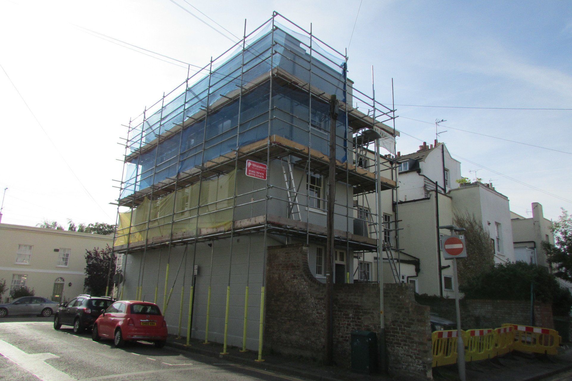 A building under construction with scaffolding and cars parked in front of it.