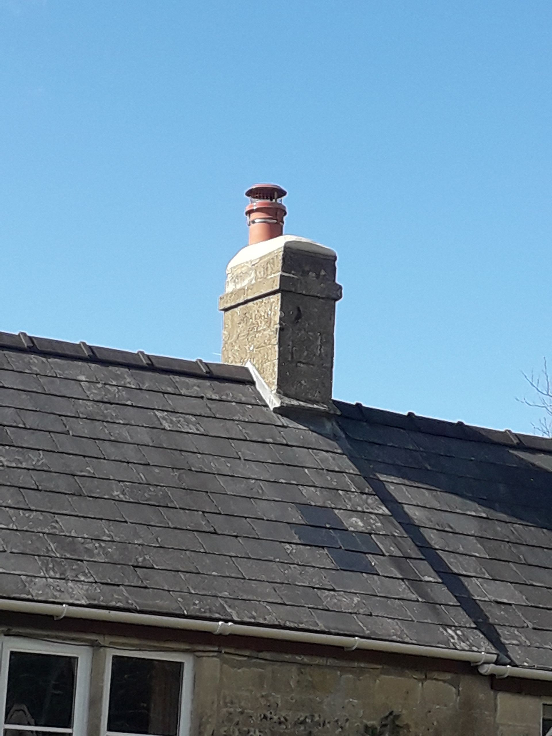 A chimney on the roof of a house with a blue sky in the background.