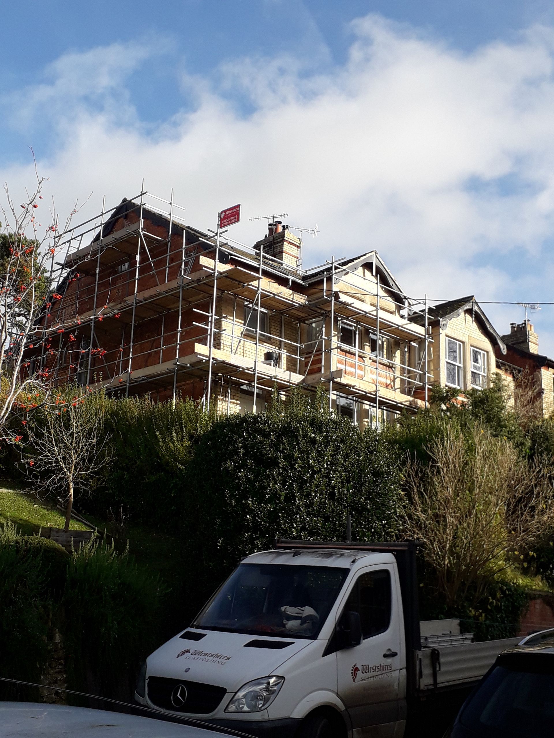 A white van is parked in front of a building under construction.