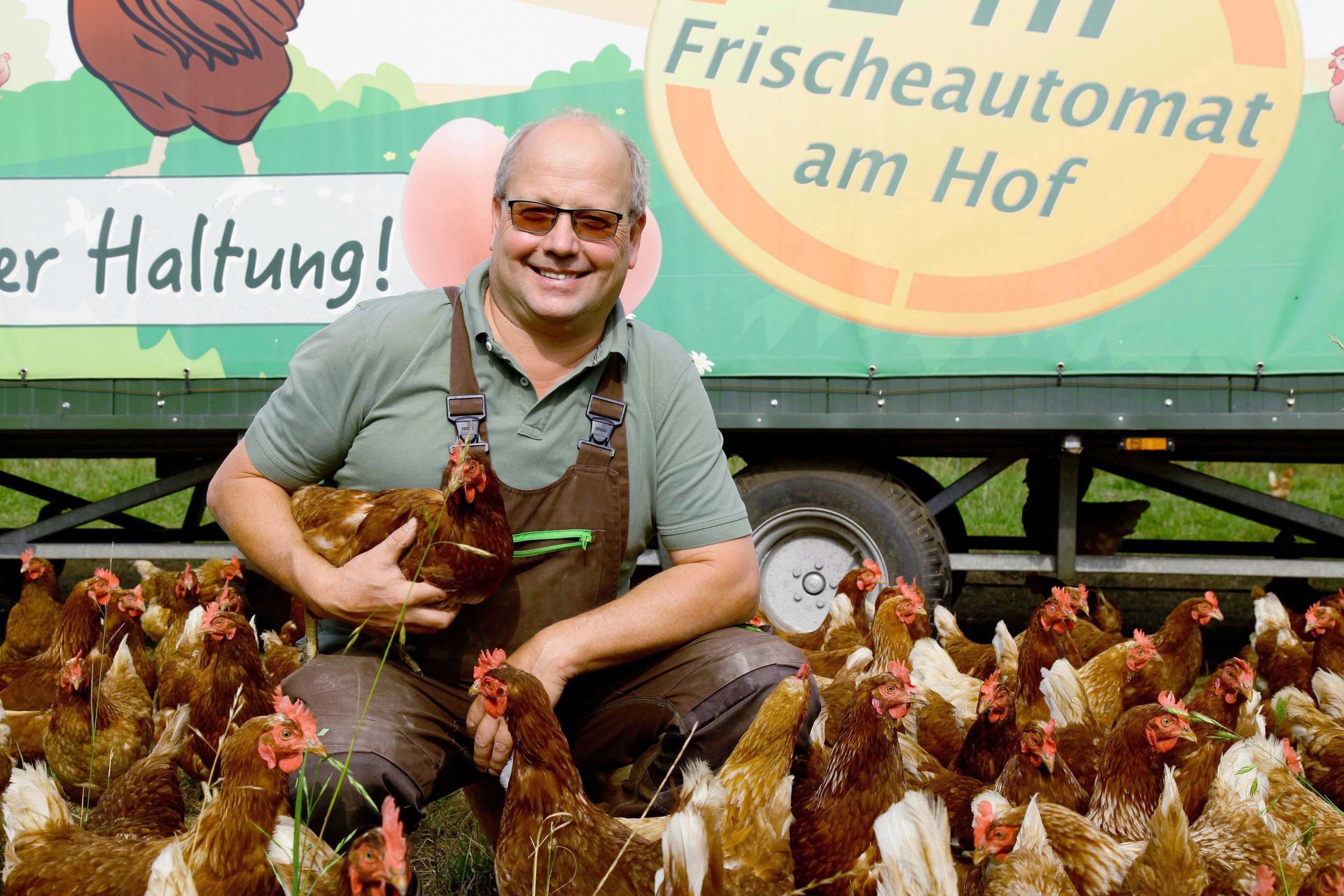Bauer Hagedorn vor dem Freilaufstall mit seien glücklichen Hühnern.