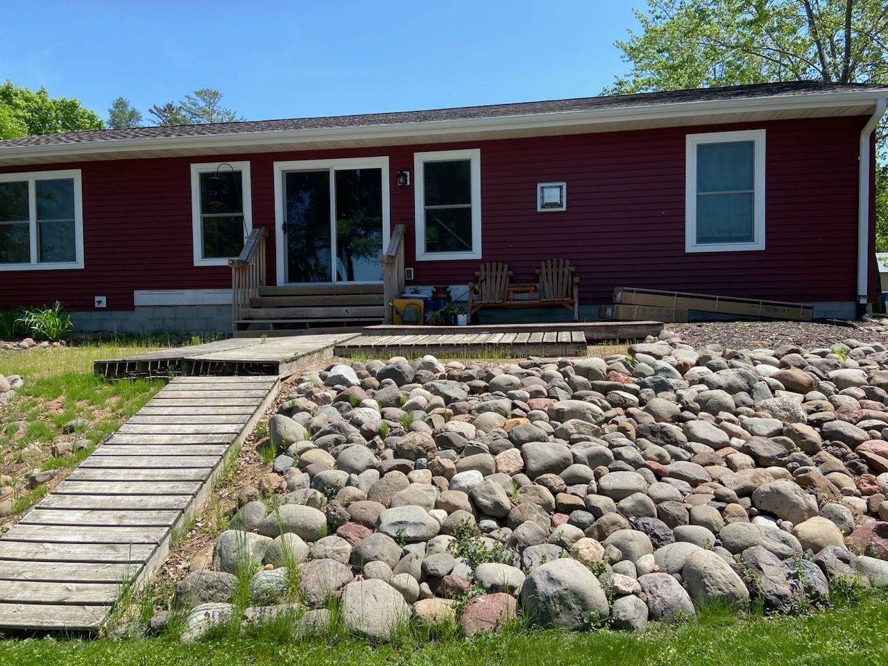 A red house is sitting on top of a rocky hill next to a wooden walkway.