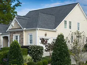 A large white house with a black roof is surrounded by trees and bushes.