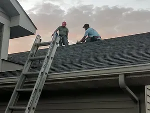 Two men are working on the roof of a house with a ladder.