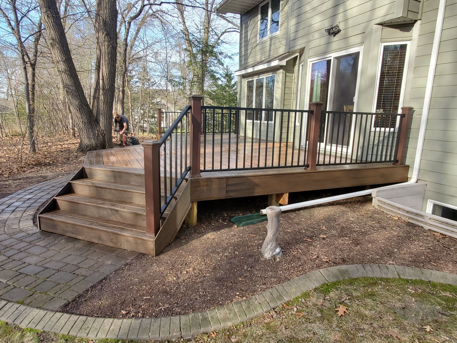A wooden deck with stairs and a metal railing in front of a house.