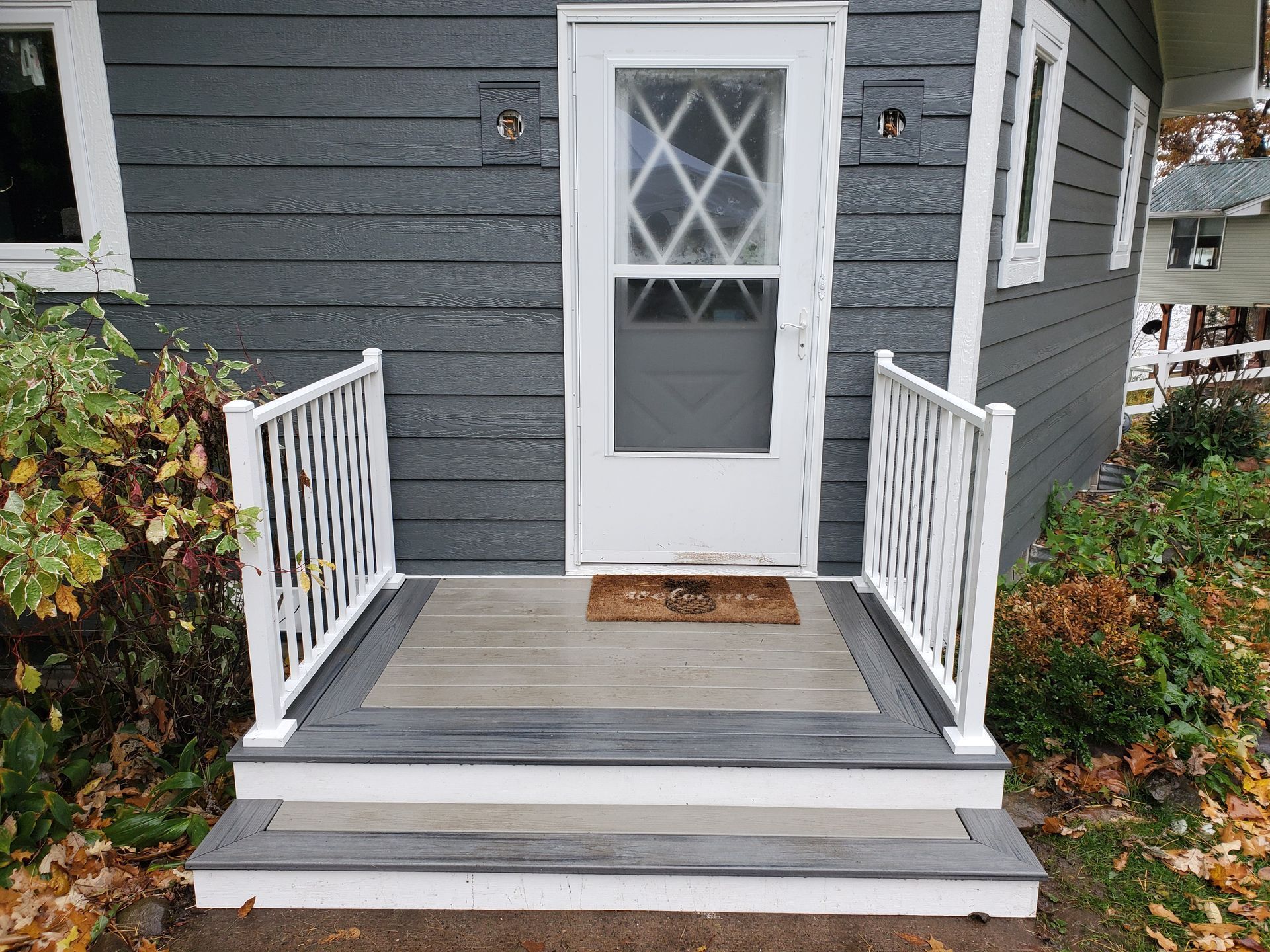 The front porch of a house with a white railing and a door.