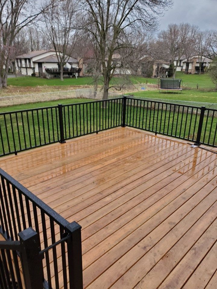 A wooden deck with a black railing and a view of a lush green field.