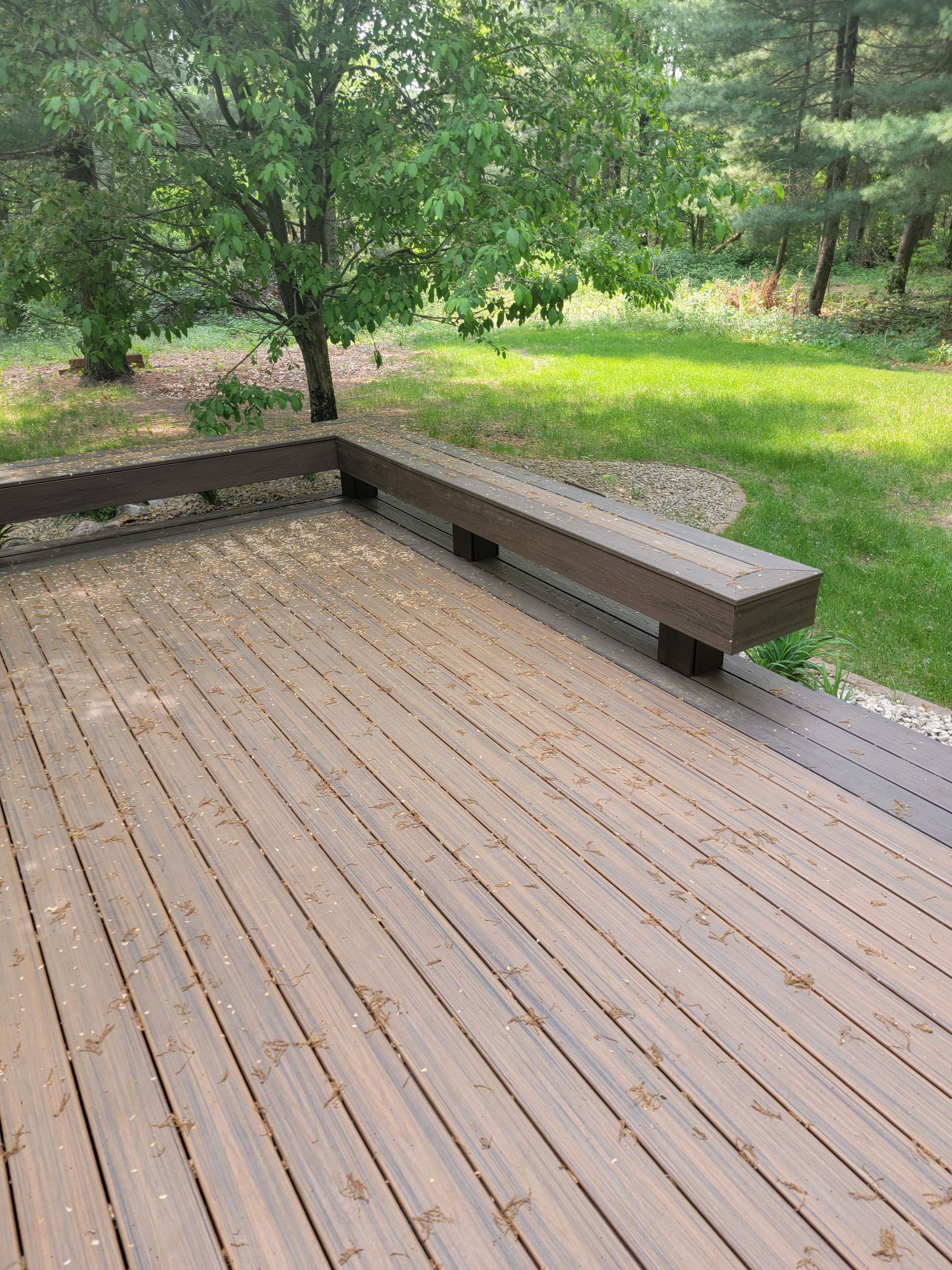 A wooden deck with a bench and trees in the background.