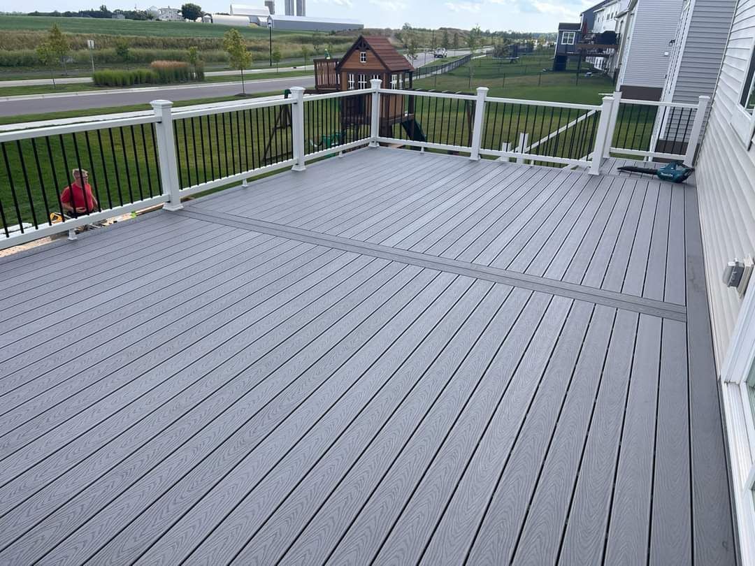 A gray deck with a white railing and a house in the background.