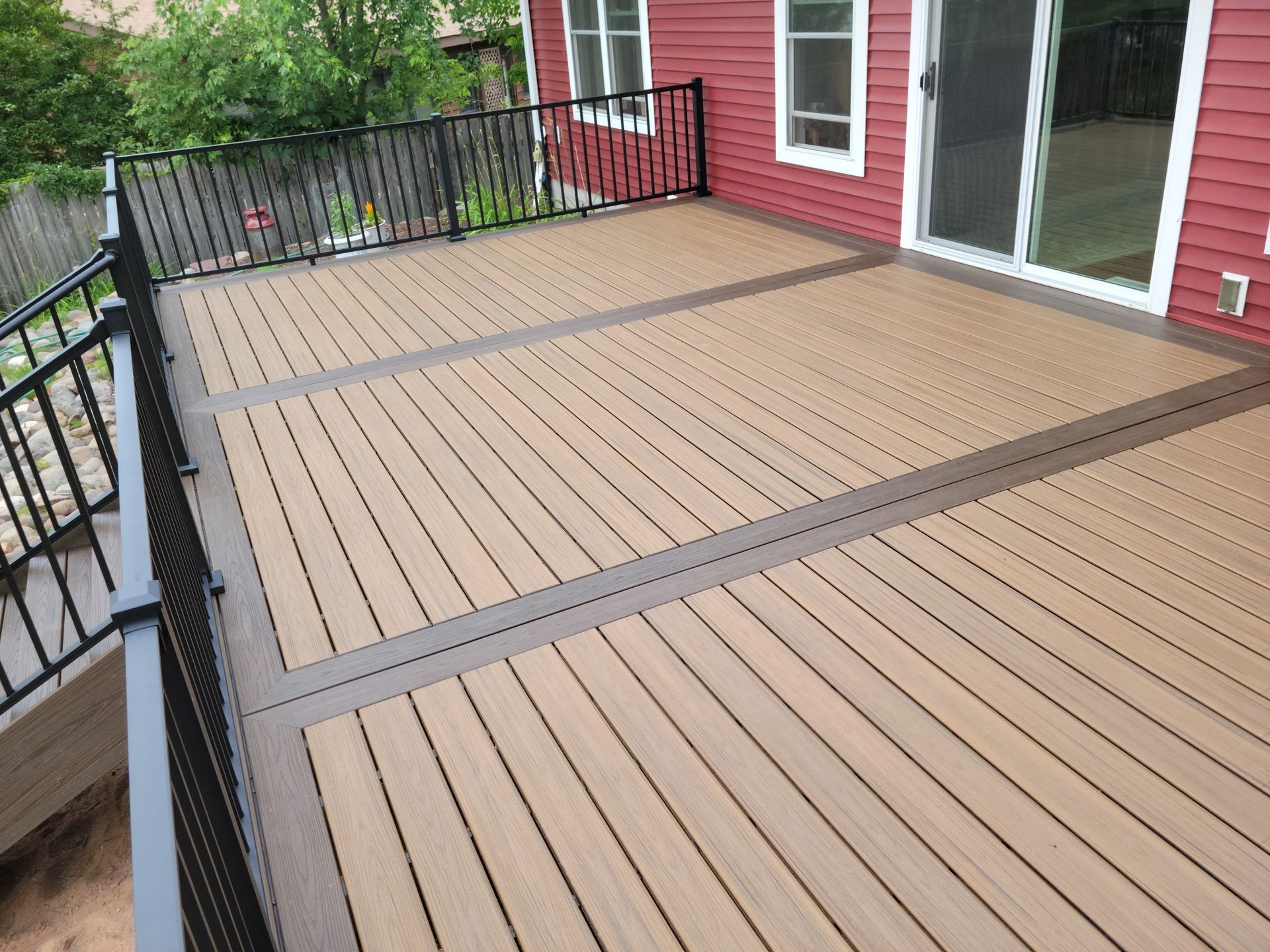 A wooden deck with a black railing and a red house in the background.