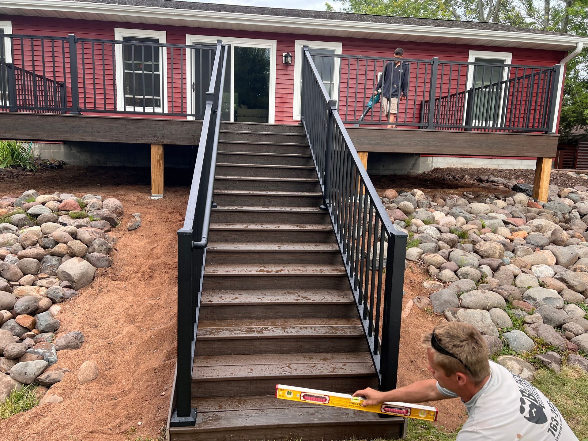 A man is measuring a set of stairs with a level in front of a red house.