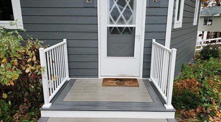The front porch of a house with a white railing and a door.