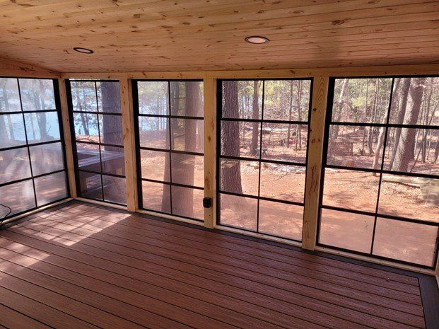 A screened in porch with lots of windows and a view of the woods.