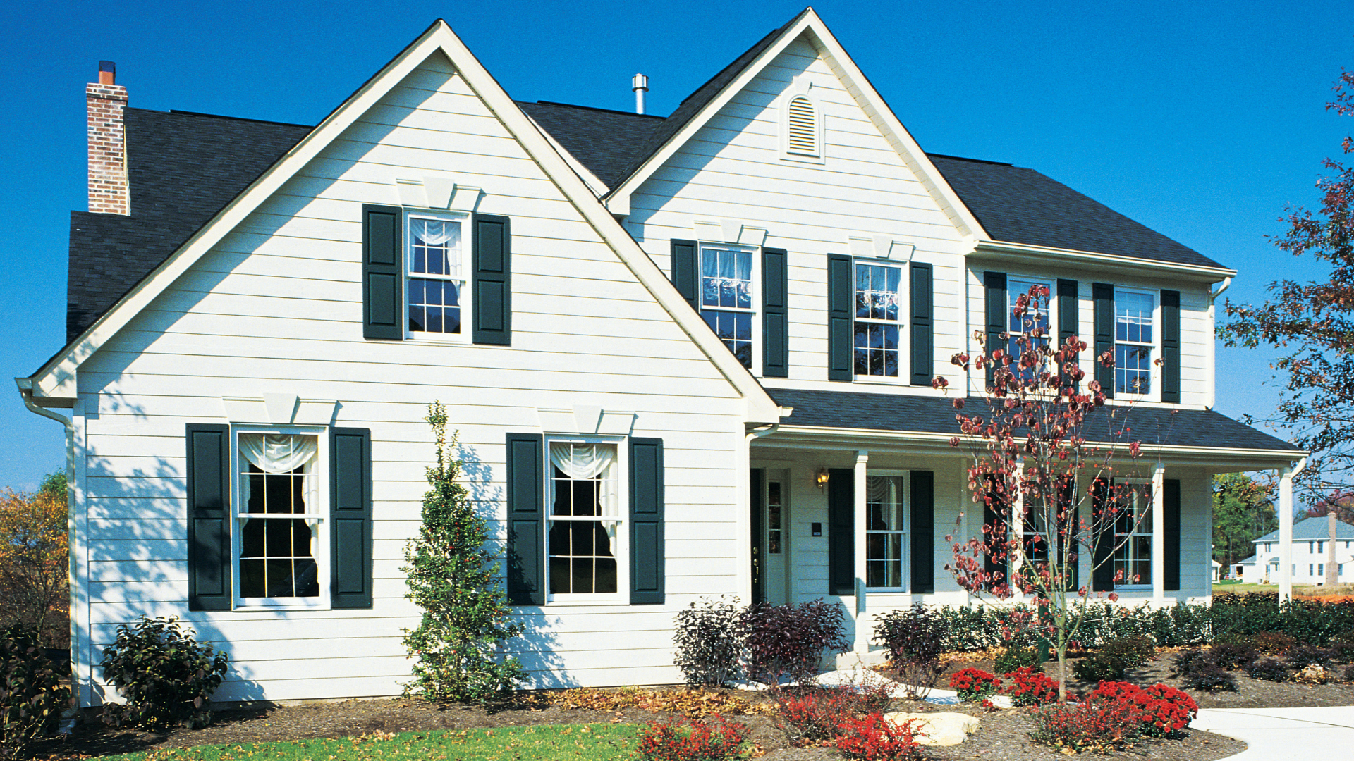 White two-story house with dark shutters and a black roof, on a sunny day.