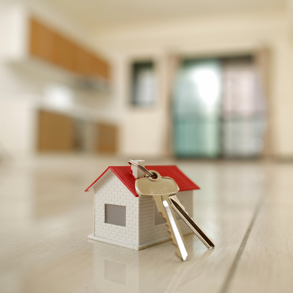 Toy house with keys on a floor, blurred interior with cabinets and a door in the background.