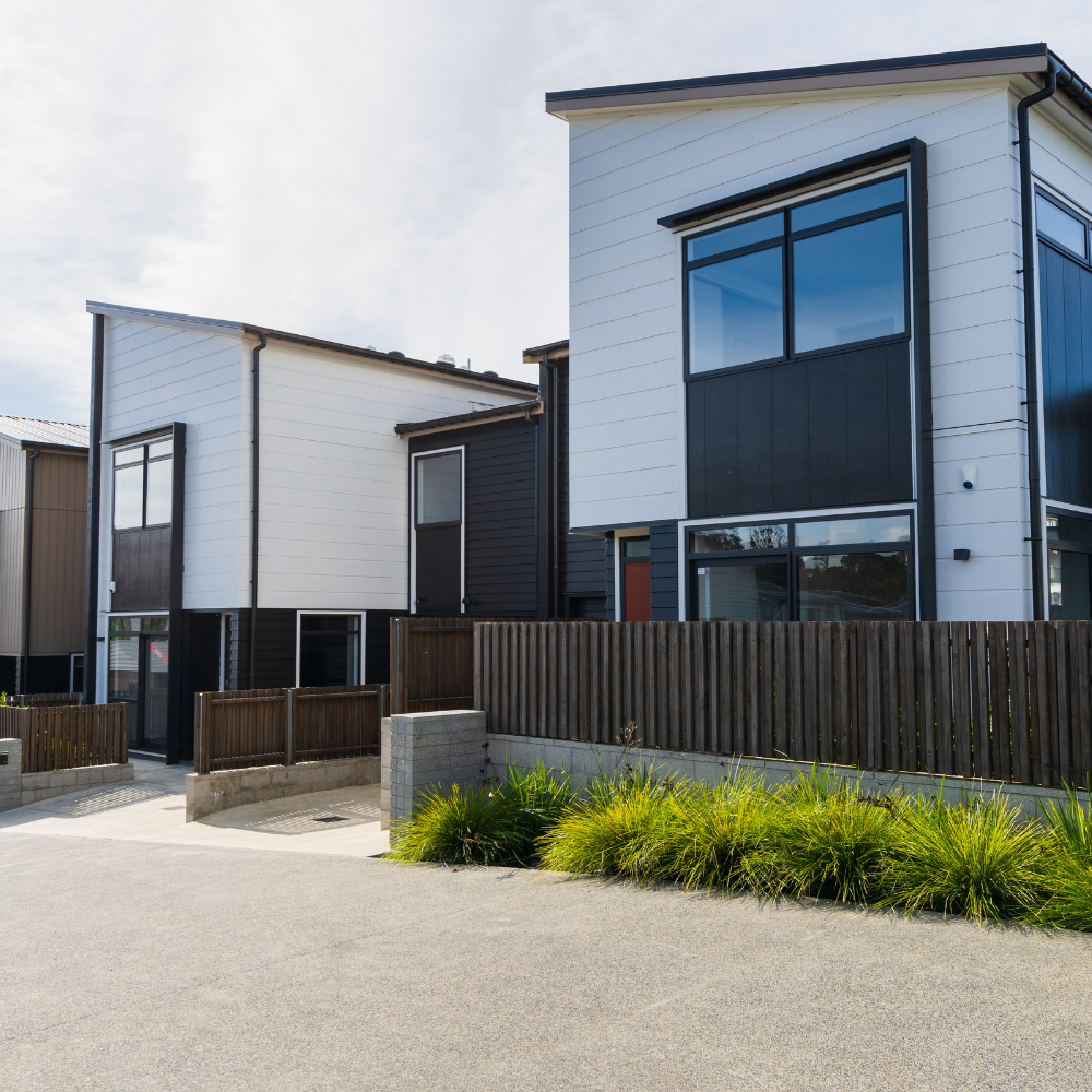 Modern townhouses with white and black siding, fenced yards, and a paved driveway.