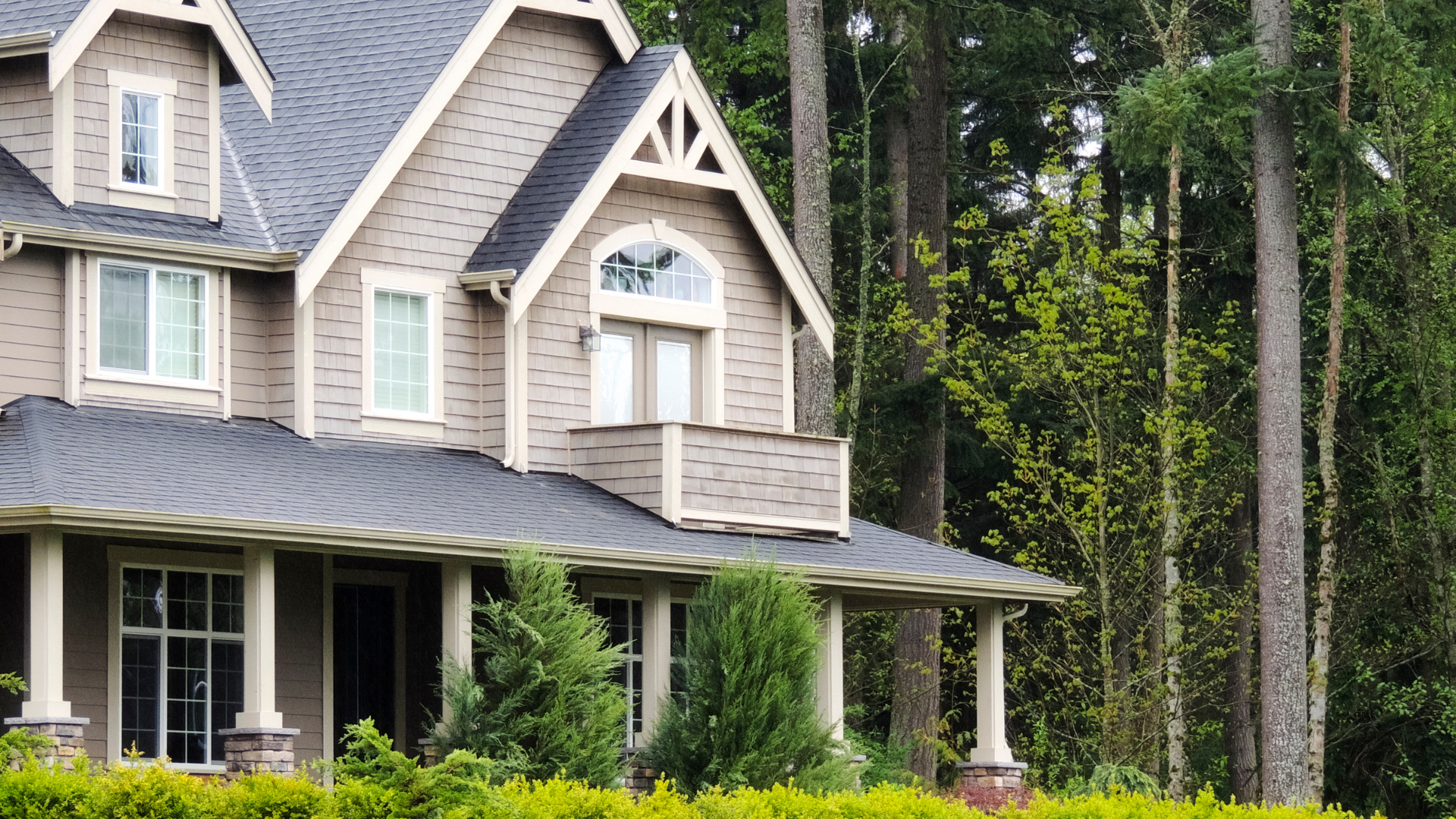 Two-story beige house with a dark gray roof, surrounded by trees.