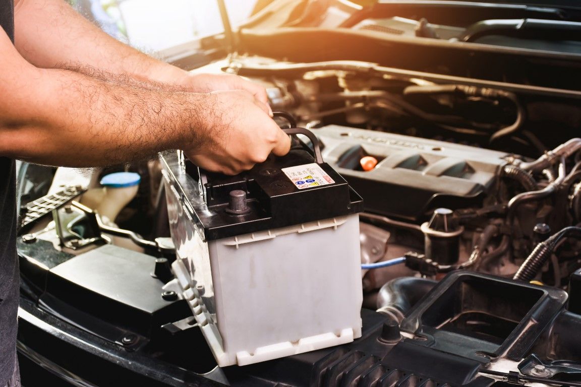 Mechanic installing a car battery in an open engine bay with a wrench