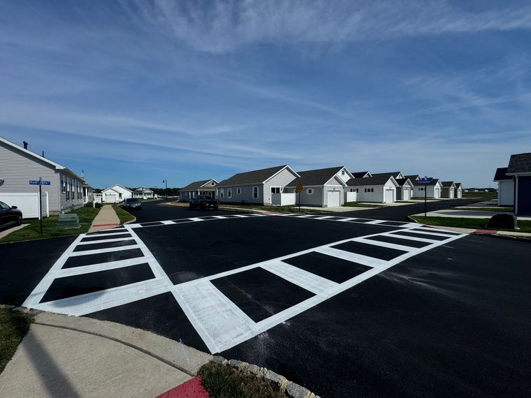 Street with houses and crosswalk on a sunny day. Black asphalt, white crosswalk lines, blue sky.