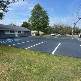 A freshly paved parking lot with white and blue lines. A one-story building is on the left, trees in the background.
