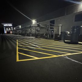 Night view of an empty car wash with yellow parking lines, black asphalt, and bright overhead lights.