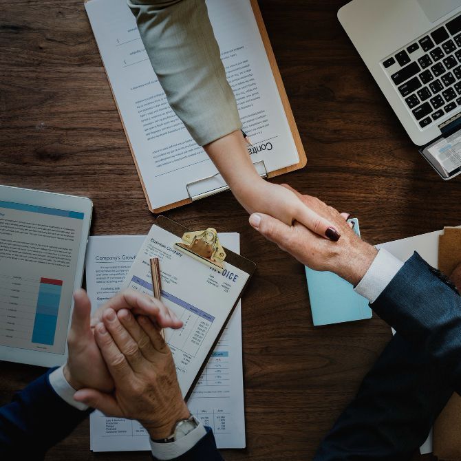 A man and a woman shaking hands over a table with papers and a laptop for Fraser Corporate Finance.