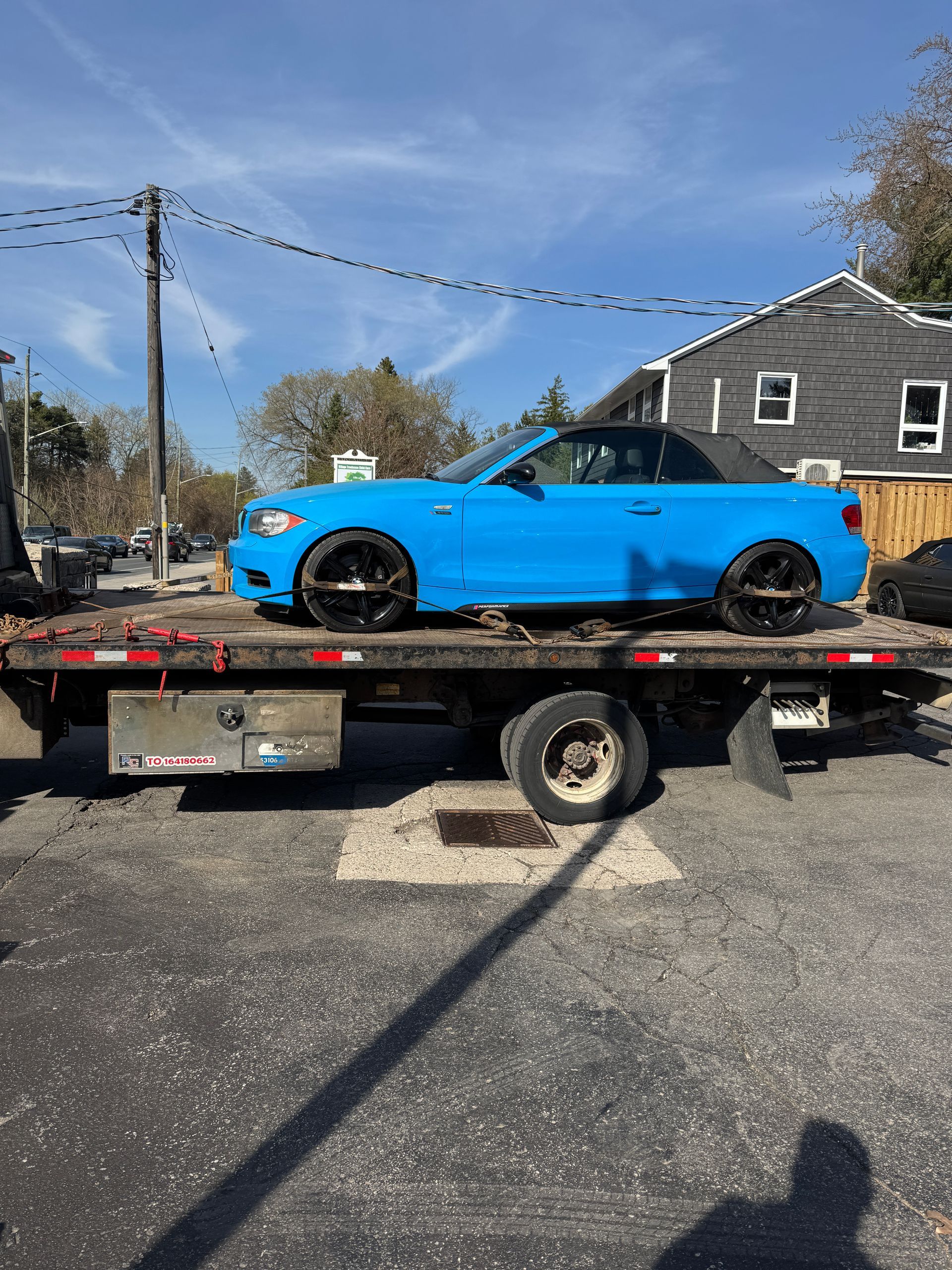 A blue BMW with black top on the back of a flatbed tow truck