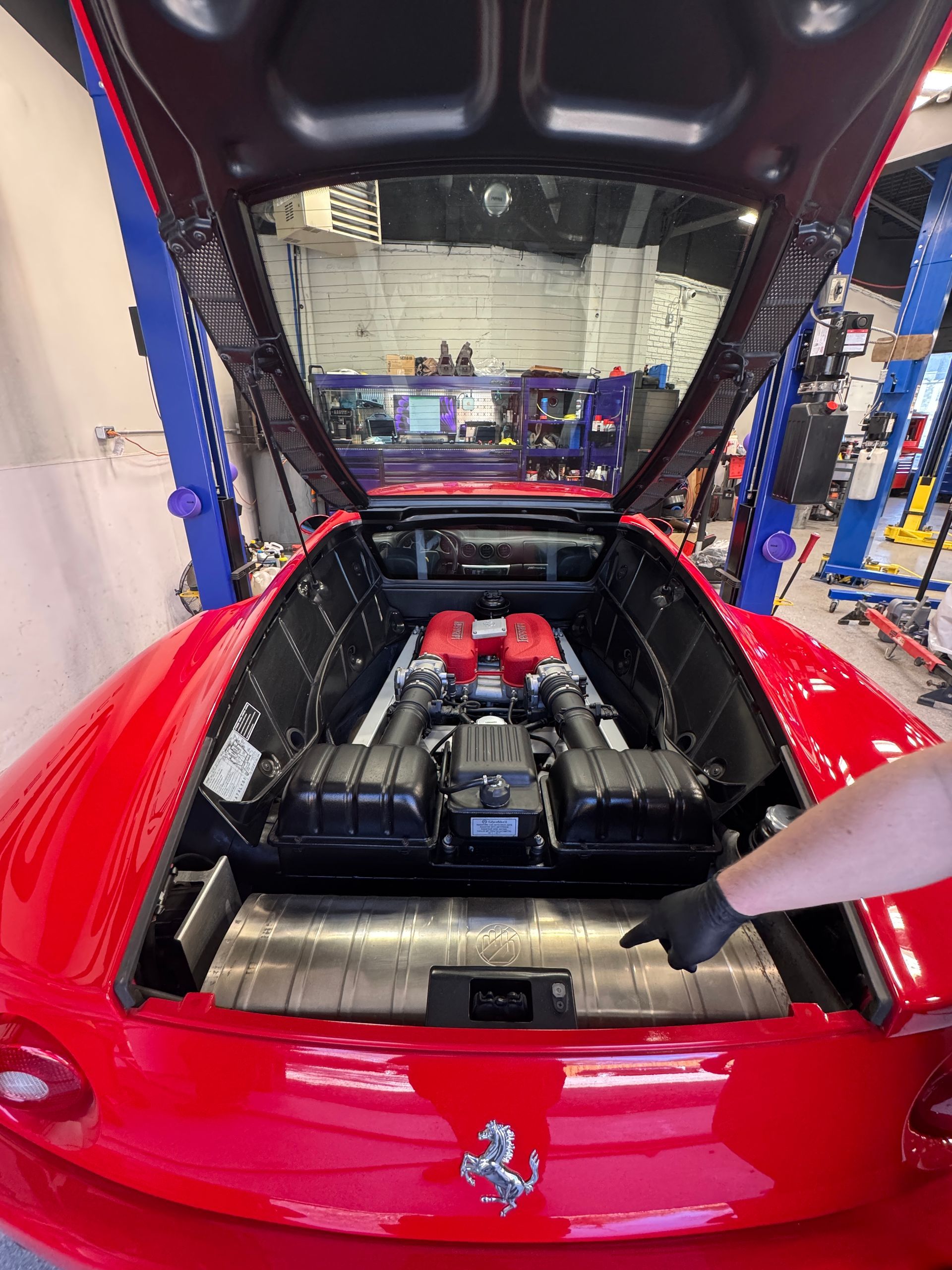 A mechanic's gloved hand pointing into the engine bay of a red Ferrari in our shop