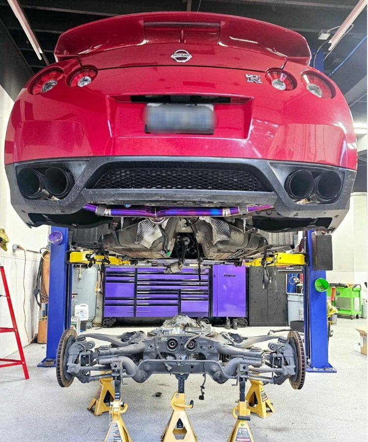 Red Nissan lifted in our shop for steering and mechanical repairs and upgrades