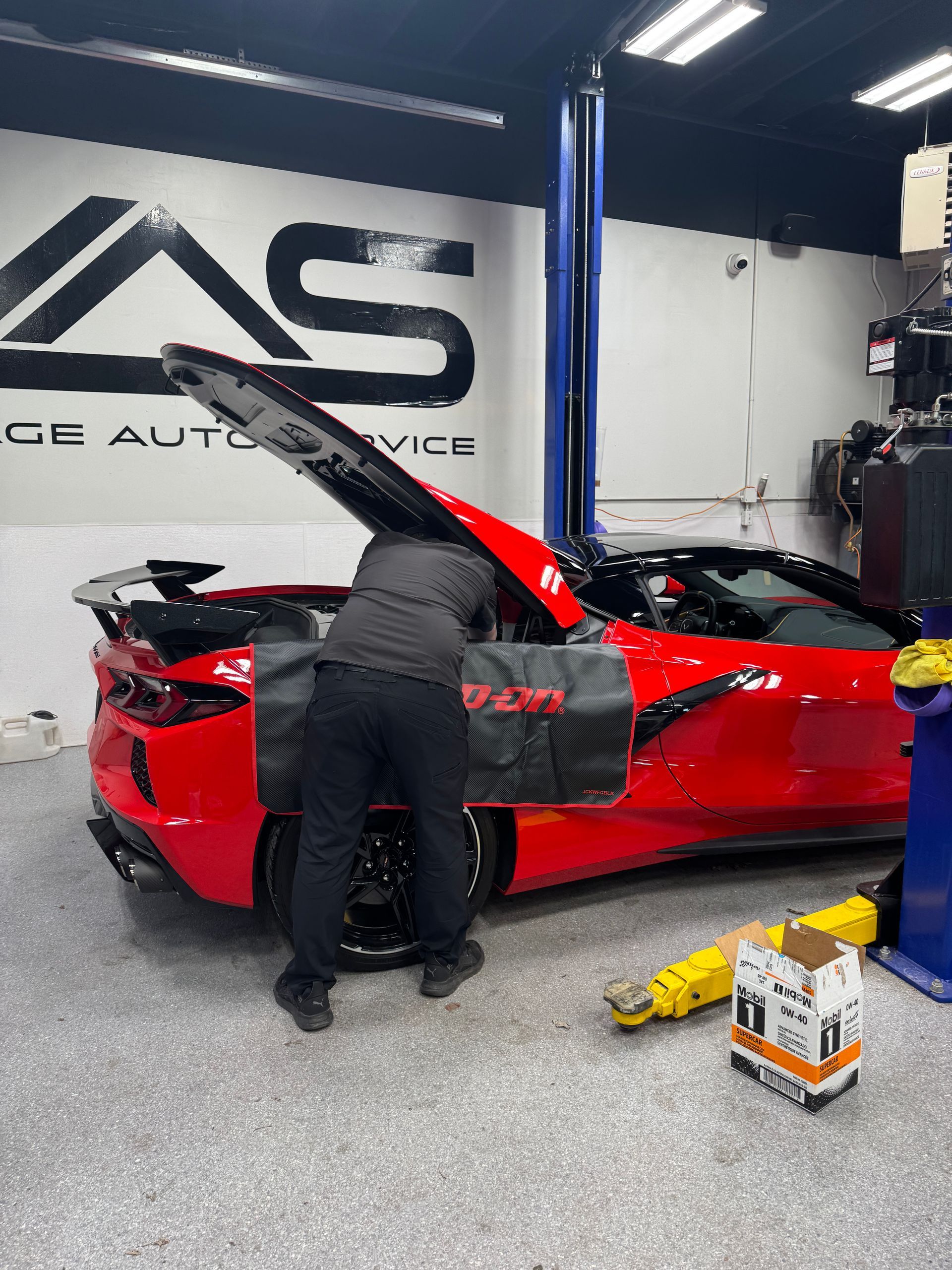 A Village Auto Service mechanic doing diagnostics and repairs on a red luxury vehicle