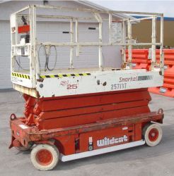 A red and white scissor lift is parked in front of a garage.
