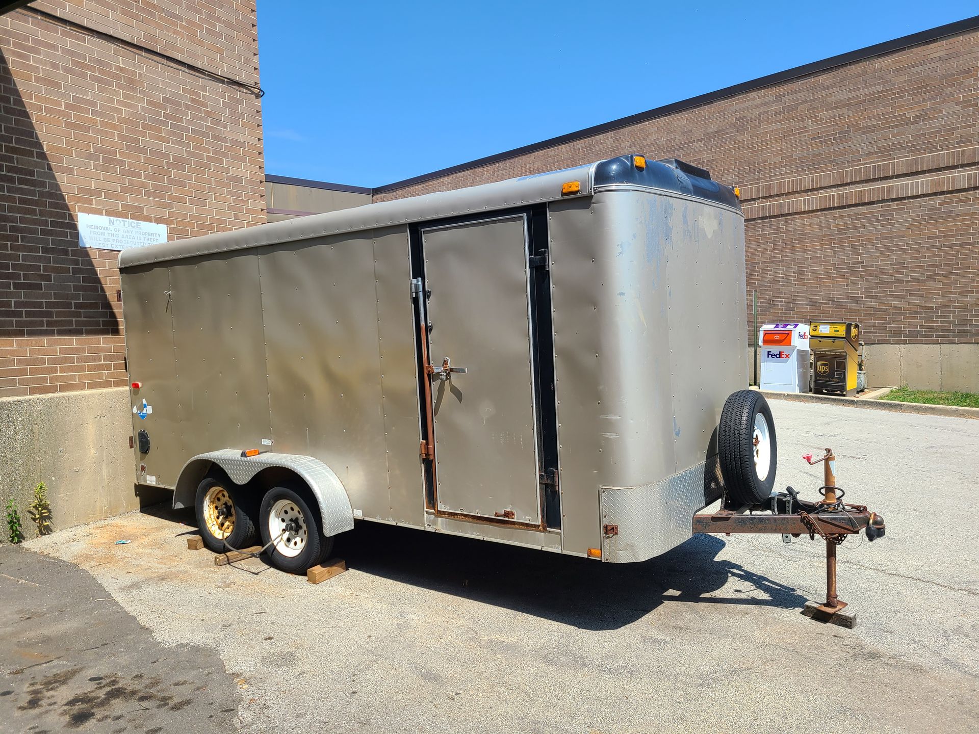 A silver trailer is parked in front of a brick building.