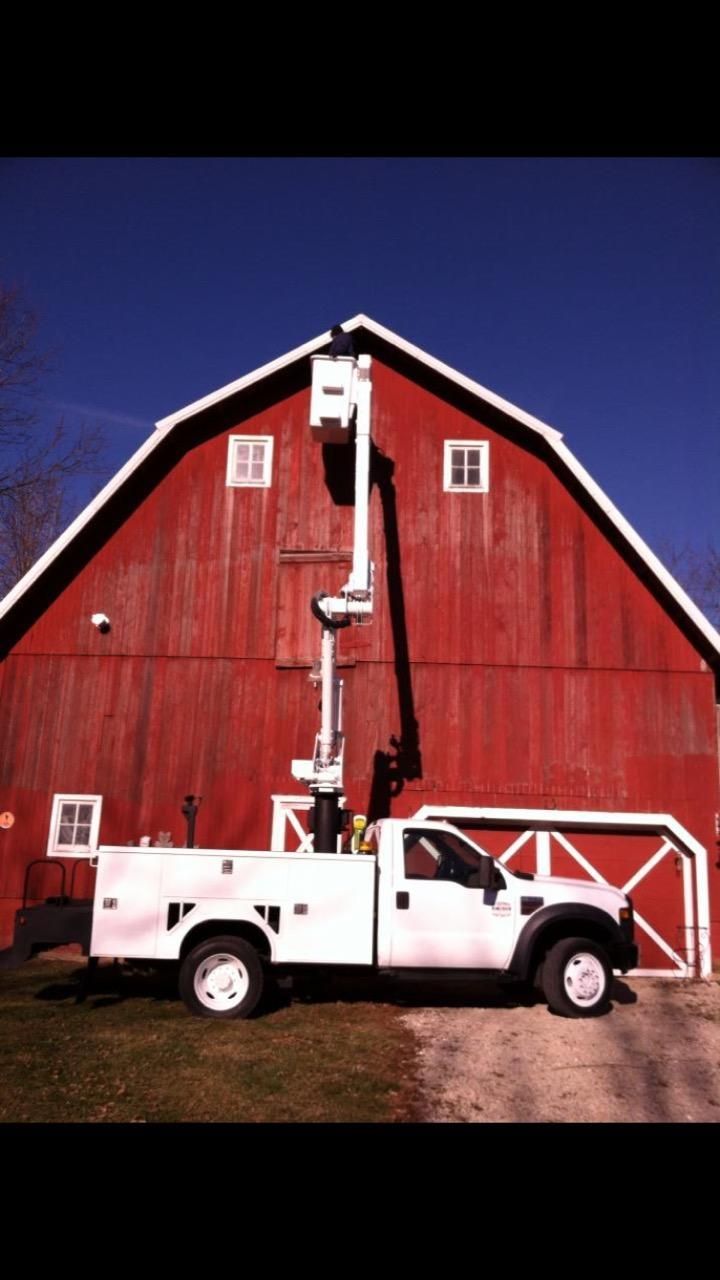 A white truck is doing operation hydraulics in front of a red barn