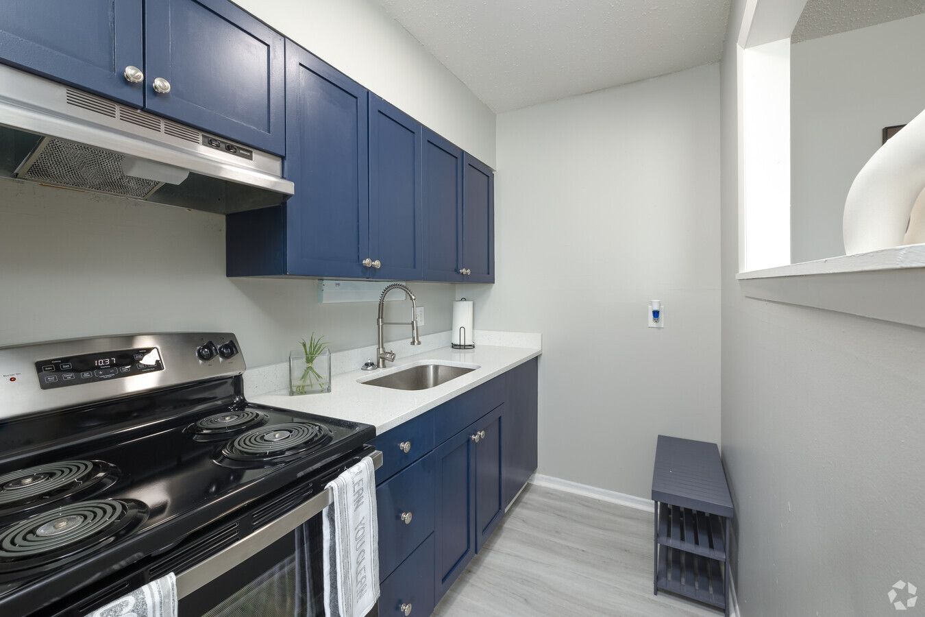 A kitchen with blue cabinets , a stove , a sink , and a shelf.
