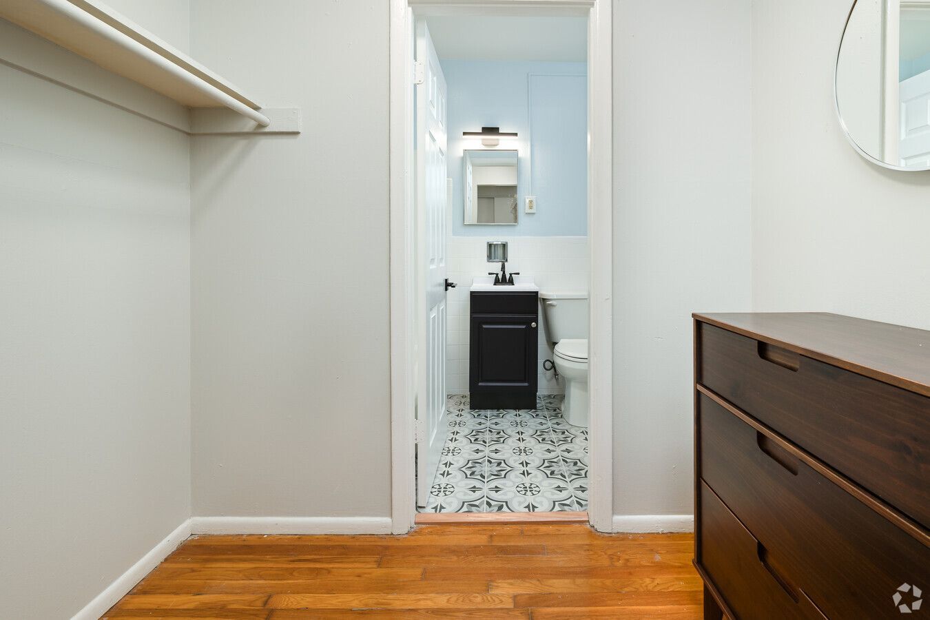 A walk in closet with a dresser and a bathroom in the background.