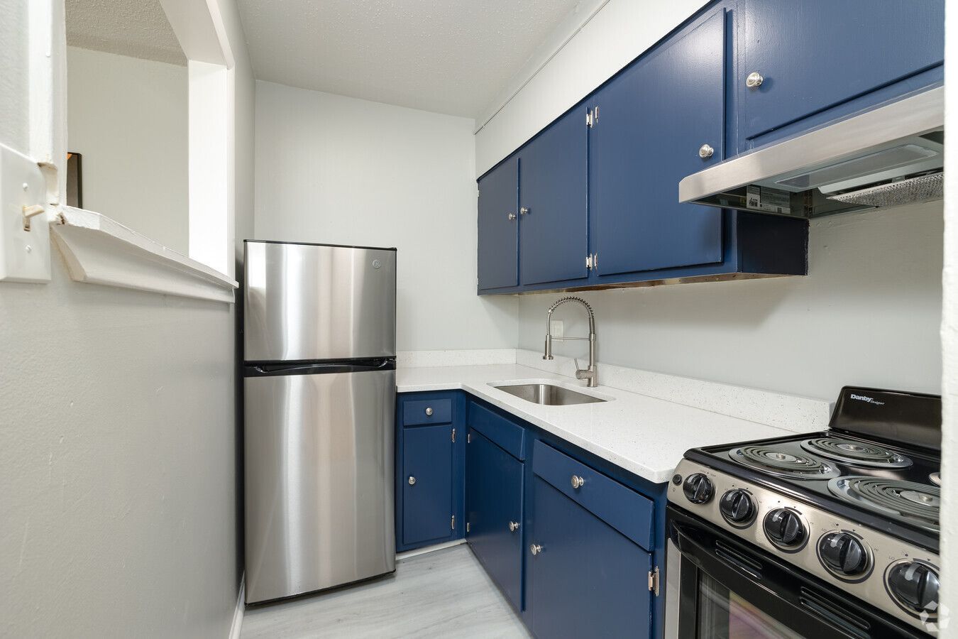 A kitchen with blue cabinets , a stainless steel refrigerator , a stove , and a sink.